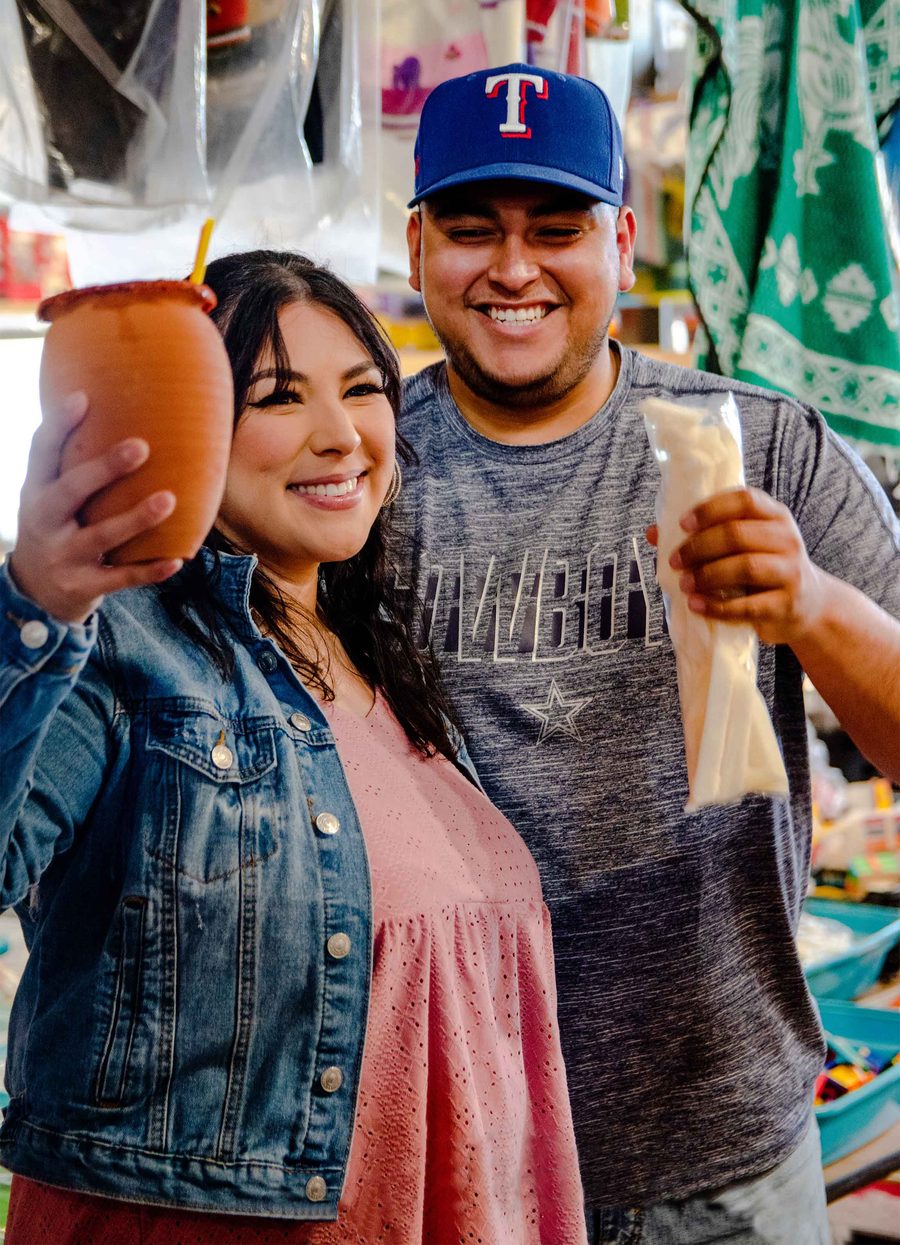 Pareja sonriente brindando con cantaritos y antojitos dentro de Azteca Farmers Market